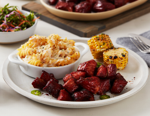 Pork shoulder burnt ends on a plate with grilled corn on the cob and pasta salad