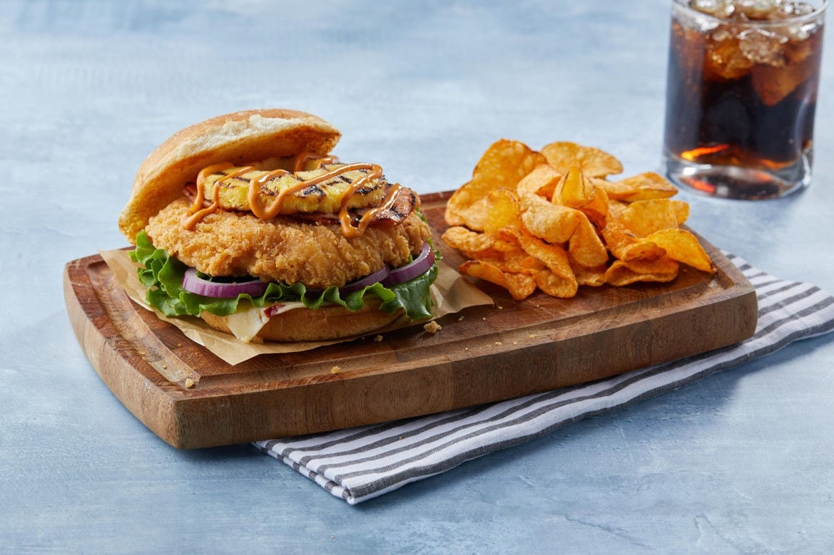 Image of sweet and spicy chicken sandwich with chips and a drink.