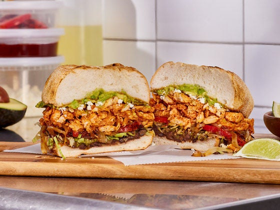 Seasoned chicken torta with avocado, black beans, tomatoes and lettuce served on a wooden board