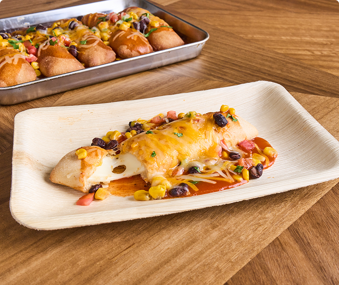 A plate with cheese breadsticks blanketed beneath enchilada sauce, melted cheese black beans and roasted corn