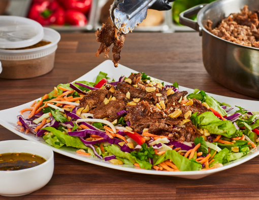 Thai Style Steak Salad topped with purple and green cabbage, red pepper, carrots, bean sprouts and peanut dressing