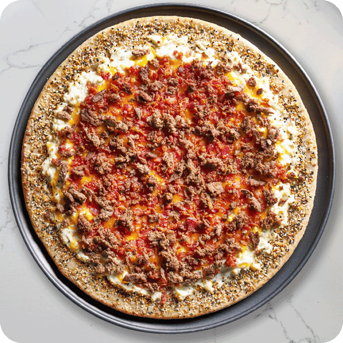 fully loaded pizza topped with egg and sliced beef on a crust with everything bagel sprinkles