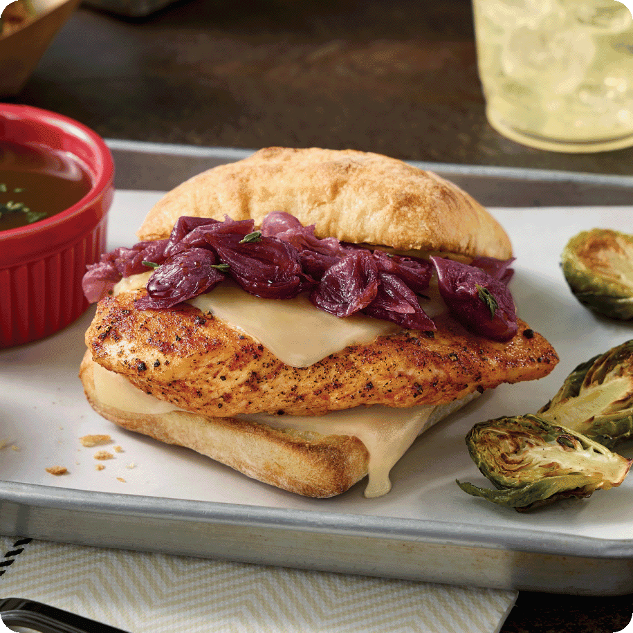 chicken sandwich with melted cheese and tender cooked onions on ciabatta roll with a side of au jus and Brussels sprouts