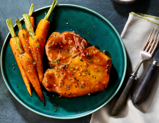 Pork porterhouse steak coated in hot honey and garlic glaze, paired with cooked baby carrots
