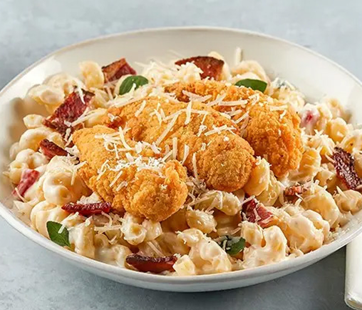 A bowl of macaroni and cheese topped with fried chicken tenders and grated parmesan cheese
