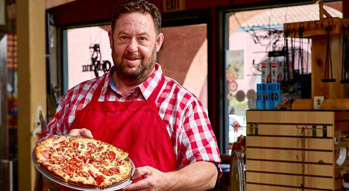 Girl with red apron holding a pizza on a wooden sleet
