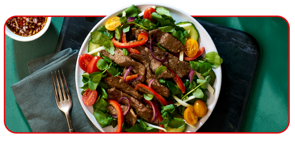 salad of greens bell pepper, tomatoes and more, all topped with sliced beef