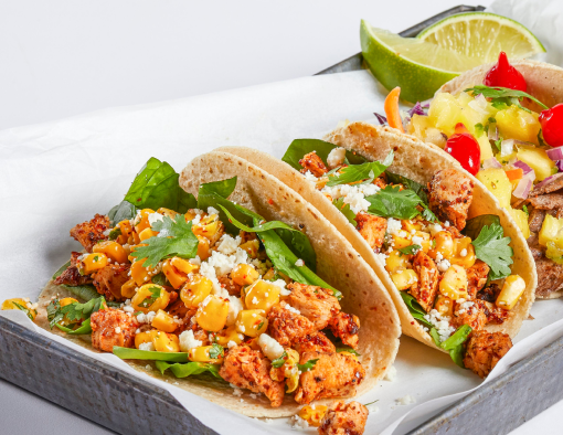 tortillas topped with elote or mexican street corn, thinly sliced avocado, red leaf lettuce and queso fresco crumbles