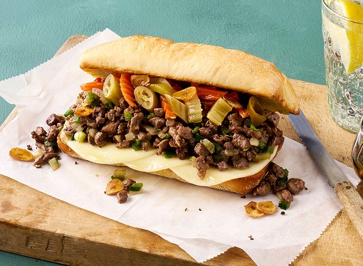 A sandwich made with chopped pepper steak and blend of sweet and spicy toppings on a French roll