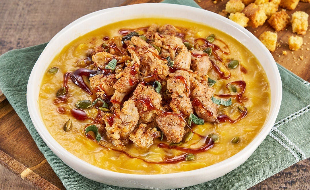 A creamy bowl of sweet potato chowder topped with croutons, pulled chicken, fried sage and a drizzle of honey