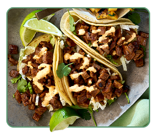 Three beef tacos with queso sauce drizzle and lime garnish on a plate