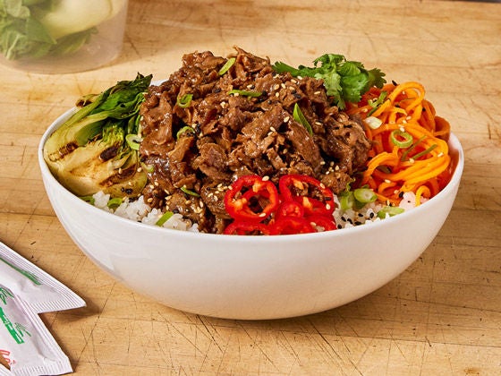 Beef steak bowl with cilantro, carrots, red peppers and bok choy, served over rice on a white bowl. 