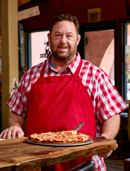 A chef standing behind a pizza
