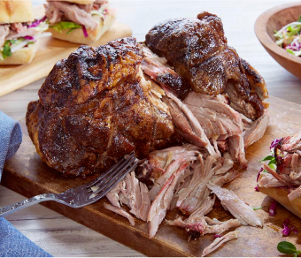 Pork shoulder on a board being shredded by fork