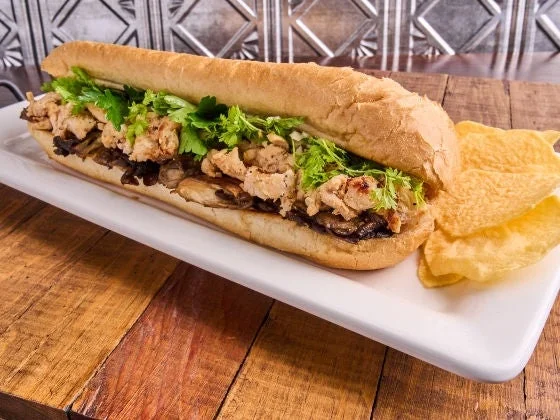 Chicken sandwich with black trumpet mushrooms, marsala vinaigrette on a hoagie roll, on a white plate