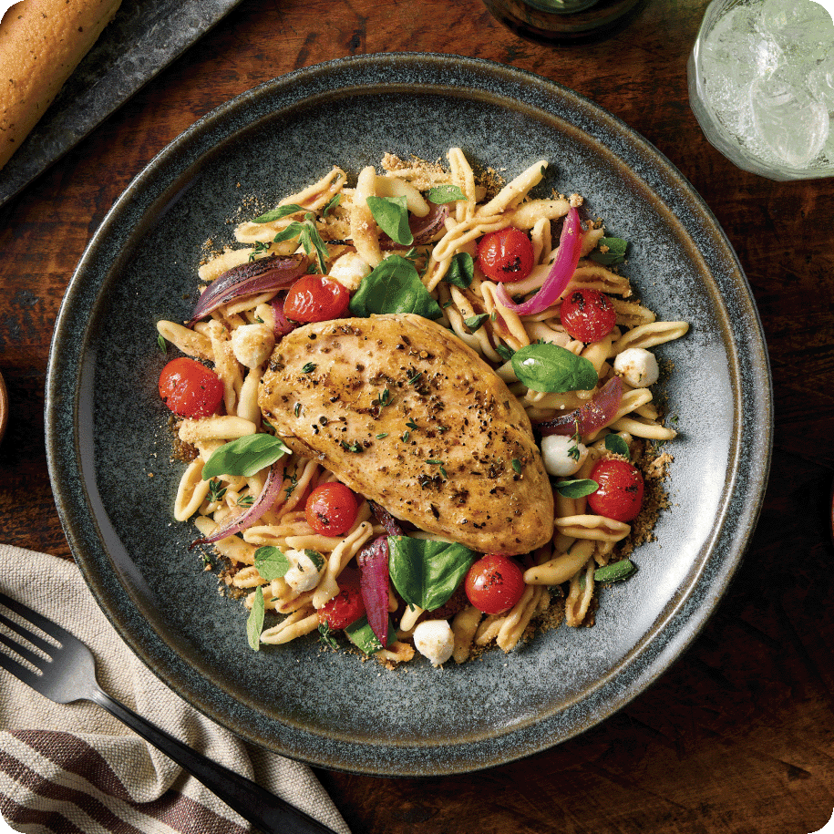 hicken breast resting on top of pasta and fresh cherry tomatoes and garnished with basil