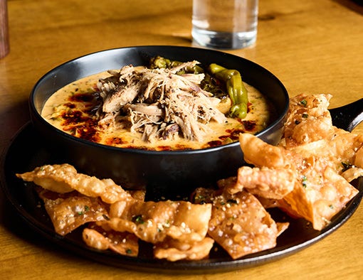 A skillet of creamy dip topped with pulled pork, served with crispy wonton chips
