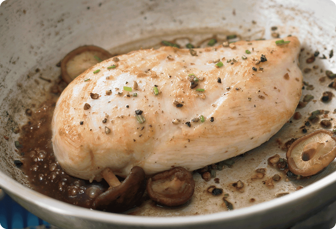A tender, juicy chicken breast cooking in a silver sauté pan with mushrooms and seasoning