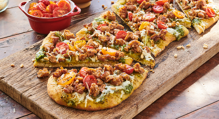 pesto flatbread sits on a wooden cutting board topped with fresh vegetables and herb-forward sauces