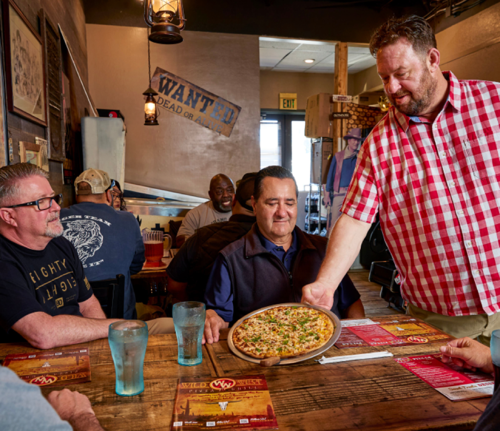 A server brings a pizza to a table of guests in a Western-themed pizza parlor