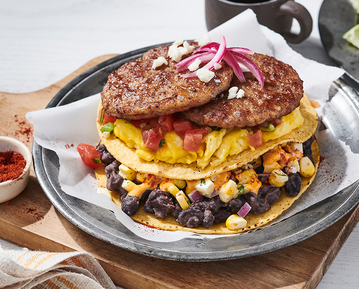 tostada stacked with refried beans, elote corn pica, sausage patties, scrambled eggs, cotija cheese and a sriracha lime crema