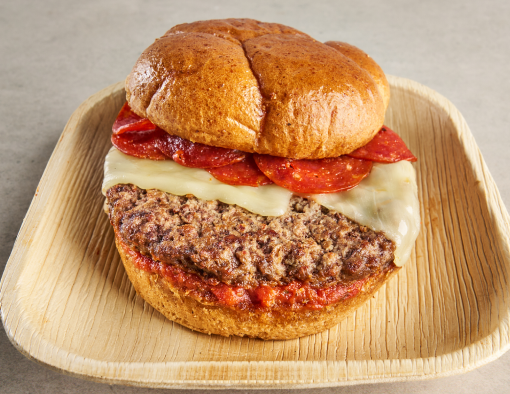 A disposable plate holding a burger with cheese, pepperoni and marinara sauce