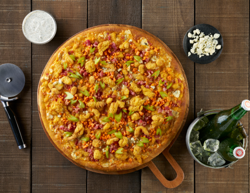 large pizza topped with buffalo cream sauce, cheddar and mozzarella cheese, Mini Chicken Bites, Bacon pieces, blue cheese crumbles and crisp pickled celery and carrots