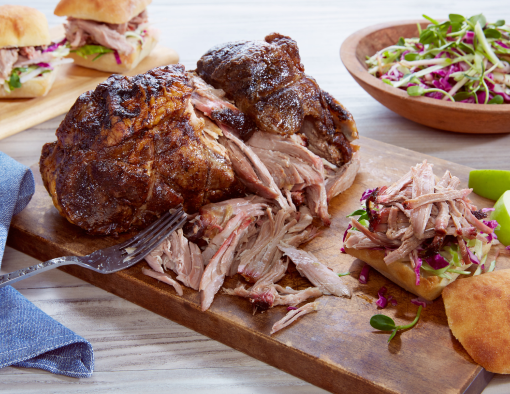 Smoked pork shoulder on a cutting board, with a bun and some pulled pork