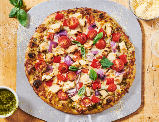 Pesto Chicken Pizza with mozzarella, tomatoes, red onions, bell peppers, and grilled chicken on a peel