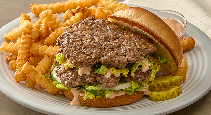 Double smashburger with shredded lettuce, onion and special sauce on a bun, served with crinkle cut French fries and pickle slices