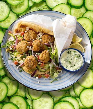pita bread with falafel and Mediterranean salad, tzatziki sauce in a cup and lemon wedges