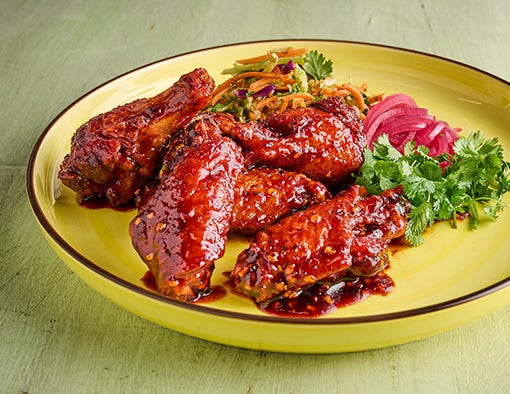 Red-sauced chicken wings on a yellow plate with coleslaw, pickled red onions, and cilantro