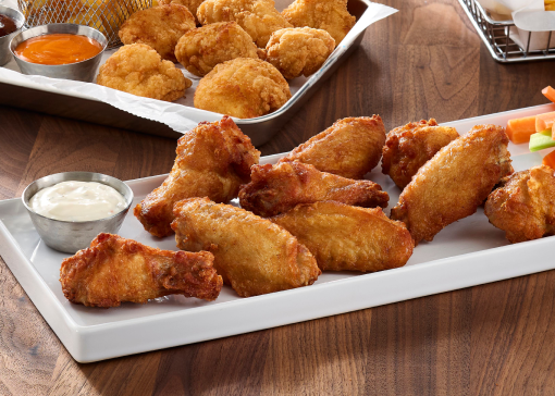 A rectangular plate of bone-in chicken wings next to a dipping sauce.