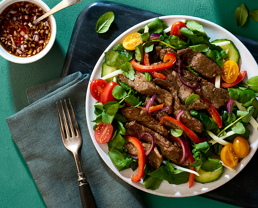 salad of greens bell pepper, tomatoes and more, all topped with sliced cooked beef
