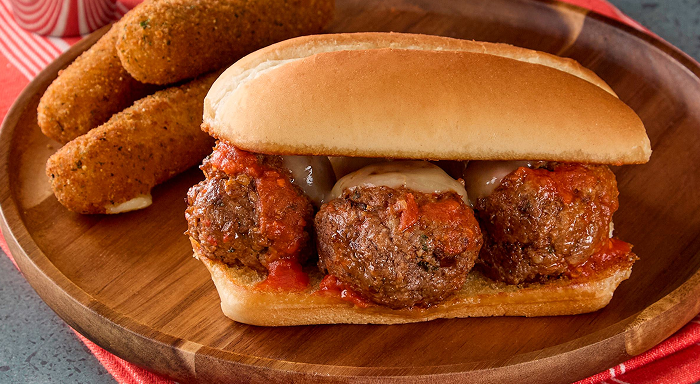 Meatball sub sandwich with marinara sauce and melted cheese on a toasted roll, served with fried mozzarella sticks
