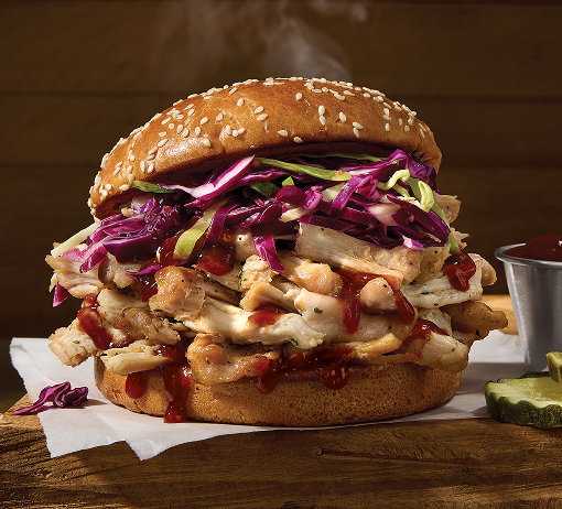 Close-up of smoked chicken sandwich on a sesame bun with sliced chicken, cheese, purple cabbage slaw, and barbecue sauce