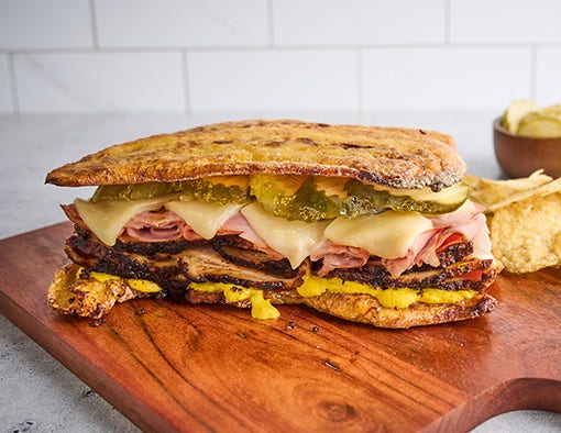 A pressed Cuban sandwich on a wooden board with chips and pickles