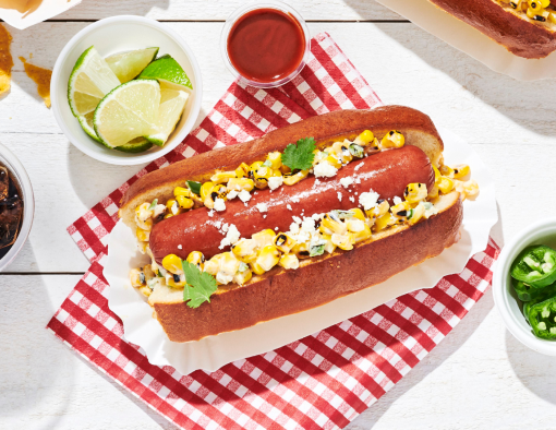 Mexican elote corn dog with corn salad, cotija cheese, and cilantro in a toasted bun on a white tray