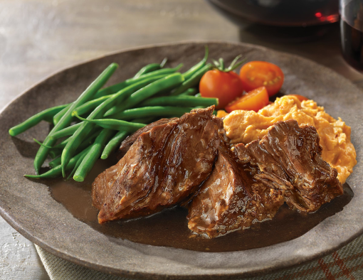 Chuck shoulder roast on a plate with gravy, green beans, mashed sweet potatoes and tomatoes