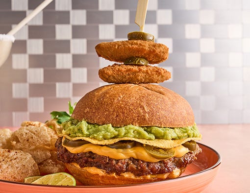 A burger with cheese, jalapeños, guacamole, and a skewer of fried jalapeños, served with pork rinds
