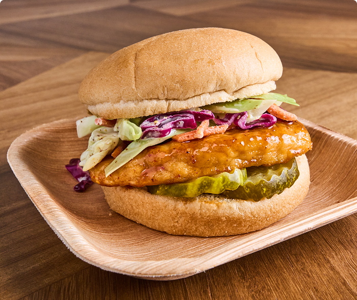 A plate with a grilled chicken patty on a whole-grain bun with sauce and dill pickles