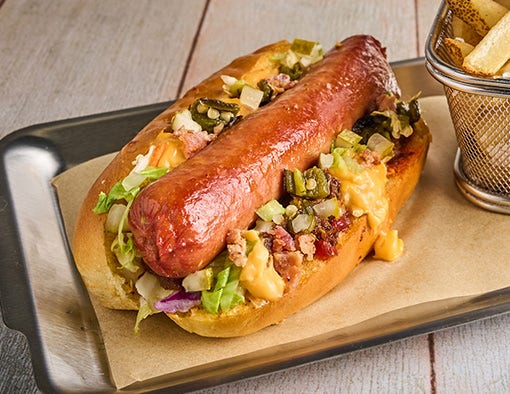 A loaded hot dog with cheese, onions, and relish on a metal tray with fries and ketchup