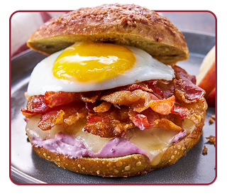 A plate with apple wedges and a cinnamon bagel sandwich with cheese, bacon and a sunny-side-up egg on top