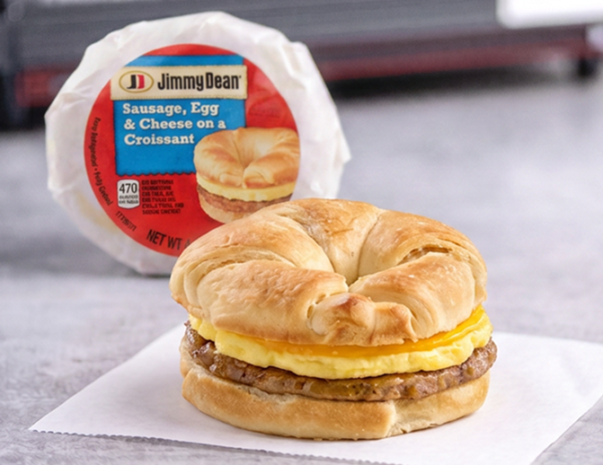 One sausage, egg and cheese sandwich standing upright in a wrapper with a second sandwich unwrapped setting on a napkin