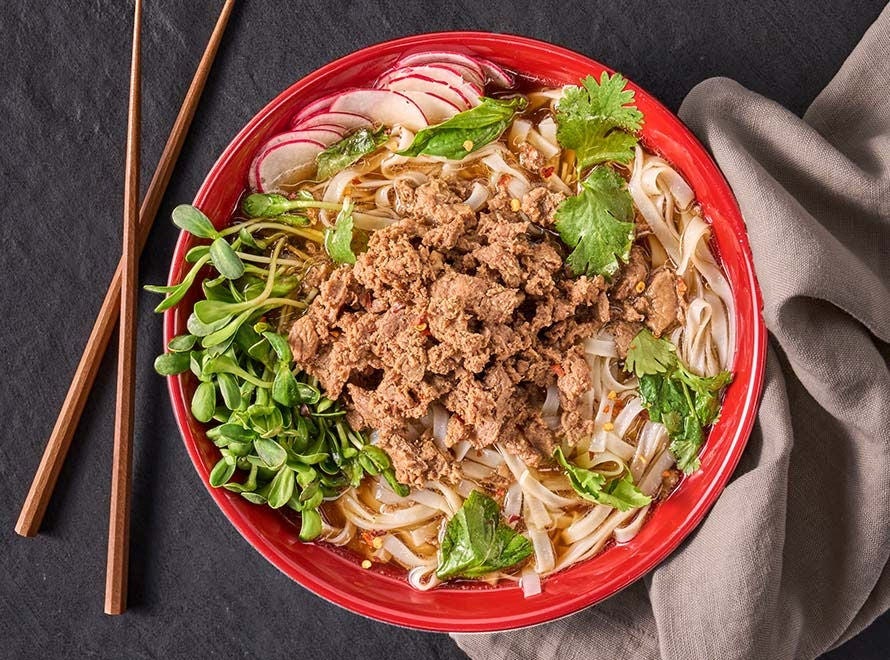 bowl of sliced beef on a bed of rice noodles with mint, basil and radishes