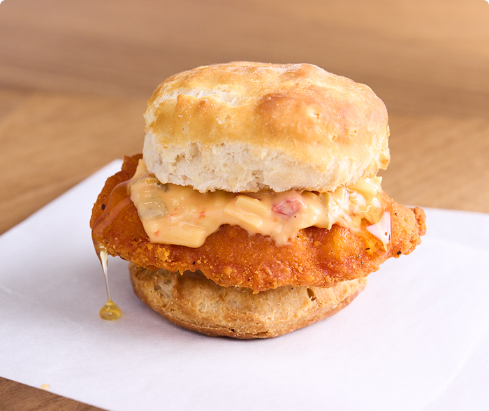 A breaded chicken filet topped with pimento cheese and honey drizzles sandwiched in a biscuit