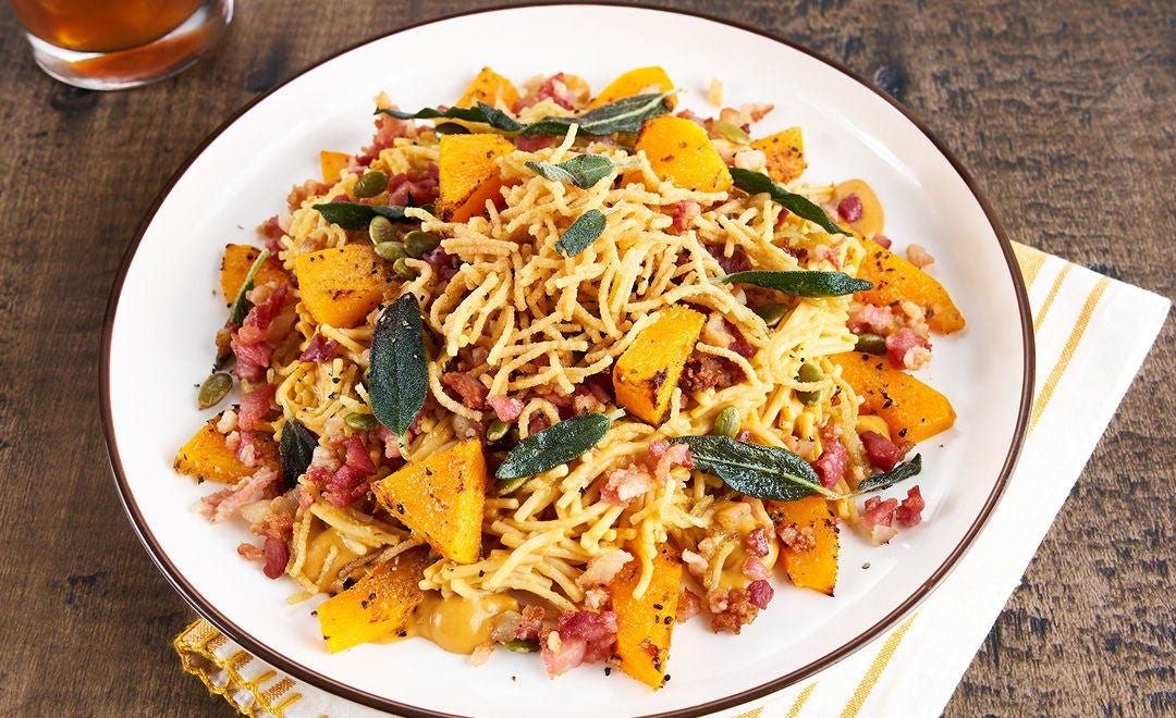 A white plate of fried pasta, butternut squash, bacon and fried sage leaves