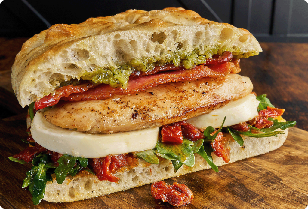 A hearty grilled chicken sandwich with tomatoes, pesto, bacon and fresh mozzarella on focaccia bread