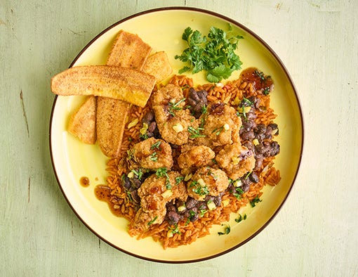 A plate of fried chicken over rice and beans with fried plantains and cilantro
