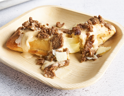 A plate with a cheese-stuffed breadstick topped with sliced steak and Alfredo cream sauce.